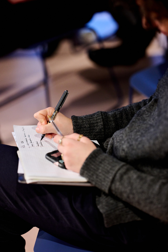 A woman making notes in her notebook writes down a sentence with a black pen in her right hand.